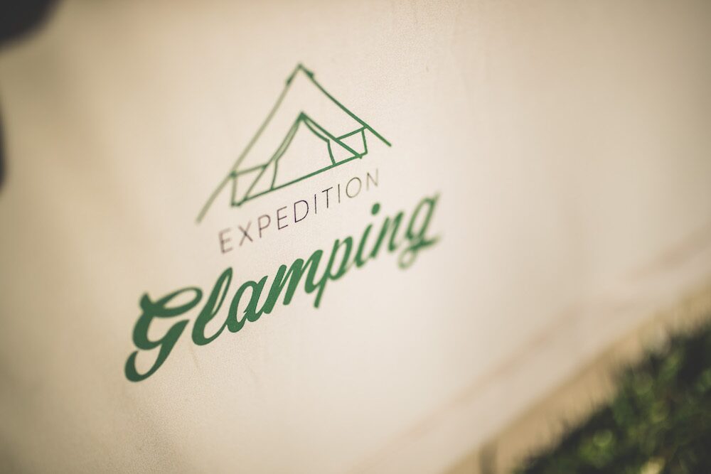 Guests relaxing in director chairs outside a furnished luxury glamping tent